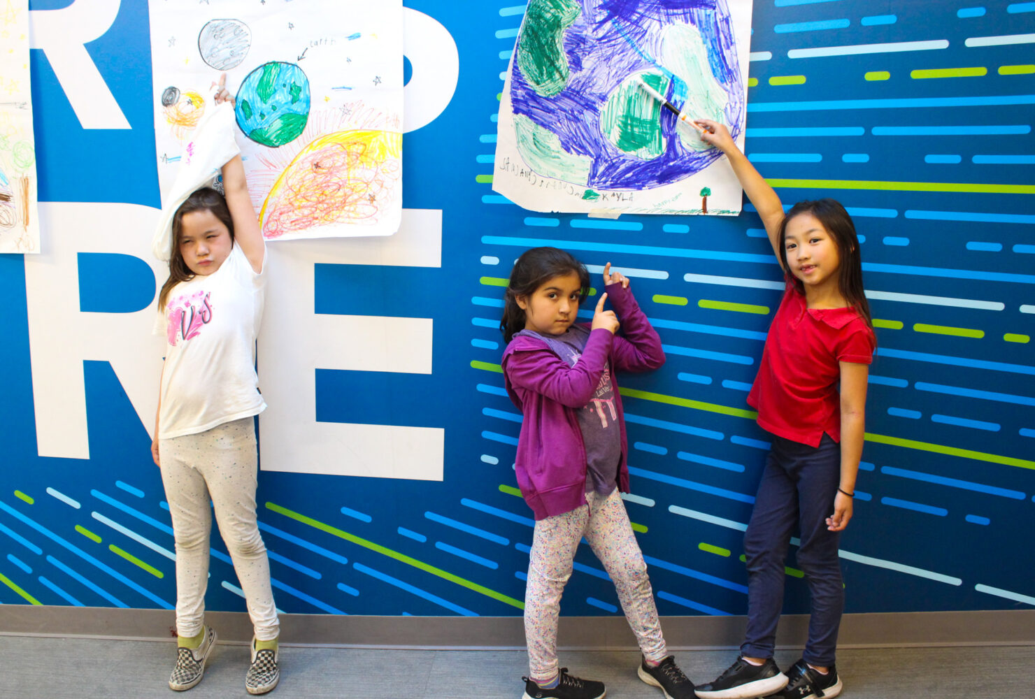 three club members pointing to their earth day posters